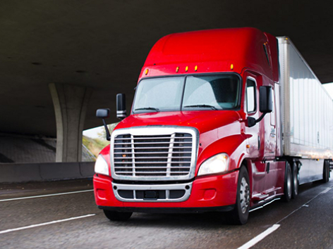 A red semi-truck is on the interstate traveling under a bridge