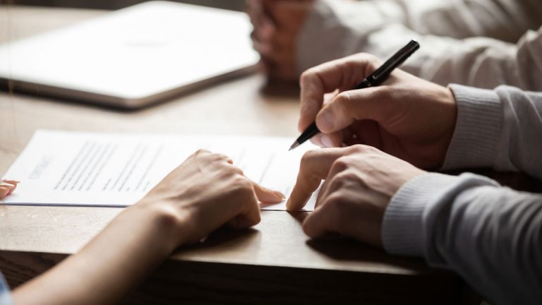 Hands are scene writing on a personal injury law contract in a board room.