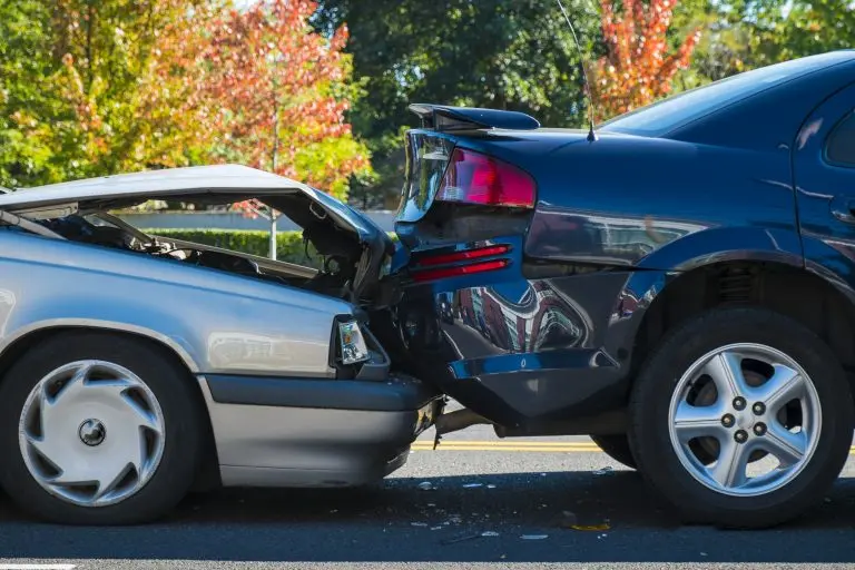 Photo of a silver car rear-ending a black car, causing property damage to both vehicles.