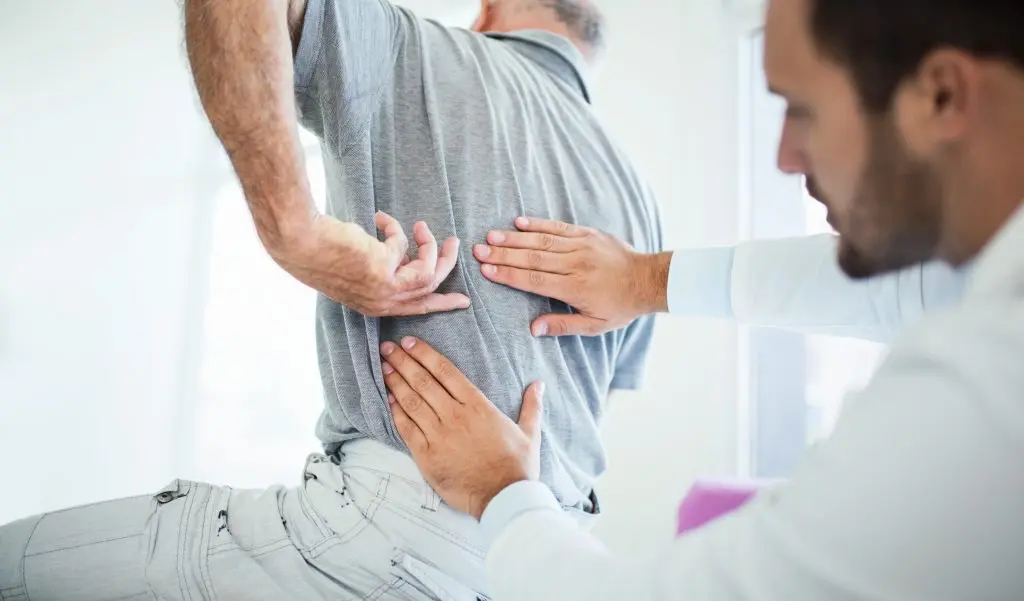 A male patient being observed my a male doctor for a work injury to his back.