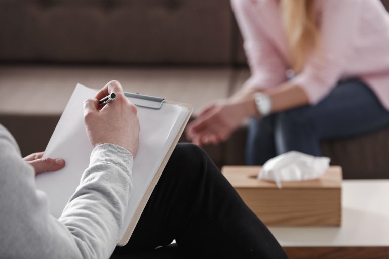Closeup of a person writing on a notepad while another person leans forward. Wrongful death can often lead to a need for therapy for family members.